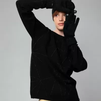 Pessoa a usar camisola preta, luvas pretas e calças bege em fundo cinza