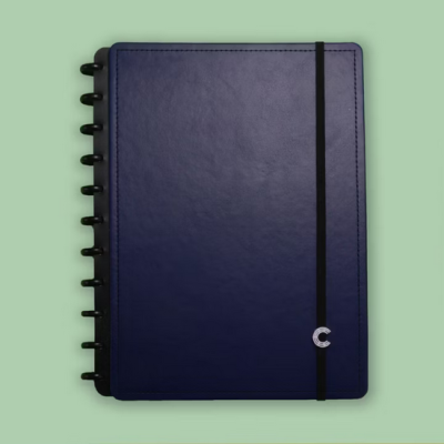 Caderno azul escuro com capa rígida, argolas pretas e elástico preto sobre fundo verde claro