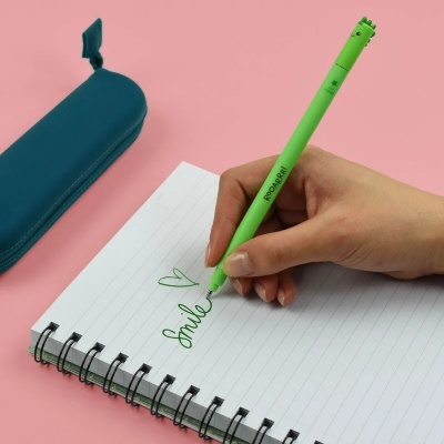 Caneta verde a escrever 'Smile' num caderno espiral branco com estojo azul ao lado