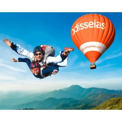 Duas pessoas em paraquedismo junto a balão de ar quente laranja com texto odisseias