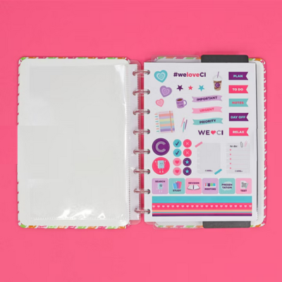 Organizador aberto com autocolantes coloridos e capa floral sobre fundo rosa.