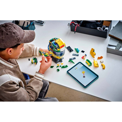 Homem a montar capacete LEGO com adesivo HONDA numa mesa branca ao lado de uma tablet com instruções