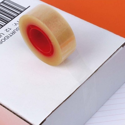 Rolo de fita adesiva transparente sobre caixa de cartão branca com etiqueta e código de barras.
