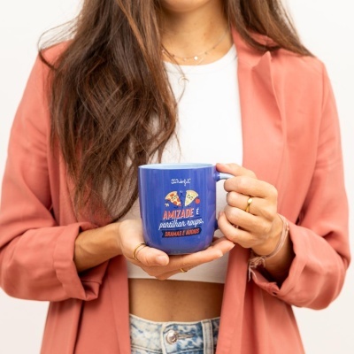 Caneca azul com texto e ilustração de pizza segurada por mulher com casaco salmão.
