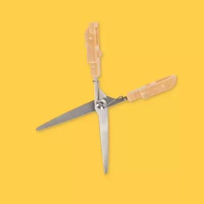 Tesoura com punhos de plástico bege em fundo amarelo