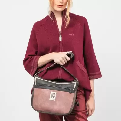 Mulher com camisa bordô e calças combinando segurando mala castanha e preta com etiqueta