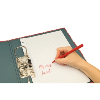 Mão escrevendo com caneta vermelha em folha pautada dentro de caderno fichário azul com argolas metálicas