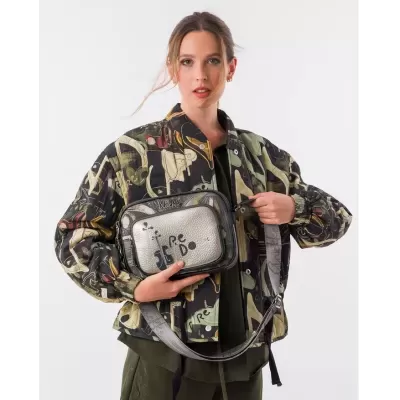 Mulher a usar casaco estampado e a segurar mala pequena prateada com texto