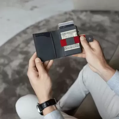 Carteira preta com cartões numa mão, sentada em sofá cinzento.