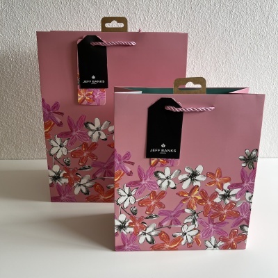 Duas sacolas de papel rosa com padrão floral e etiquetas pretas