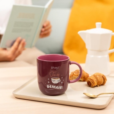 Caneca roxa com frase motivacional, bandeja com folhados, colher dourada e cafeteira branca, cenário acolhedor de leitura.