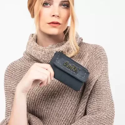 Carteira preta pequena com inscrição dourada segurada por mulher com suéter castanho