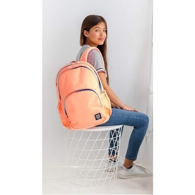 Jovem com mochila cor de salmão com detalhes cinza sentada numa cadeira branca