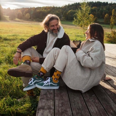 Um casal sentado num deque de madeira ao ar livre, com meias amarelas com padrões de animais e roupas de inverno.