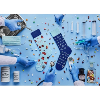Dois pares de meias médicas com padrões coloridos rodeadas por medicamentos e equipamentos em fundo azul