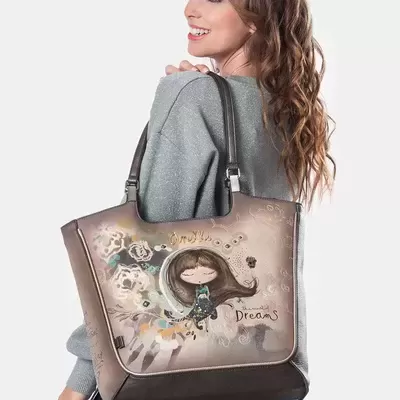 Mala castanha decorada com ilustração de menina e flores com texto Dreams ao ombro de mulher com suéter cinzento