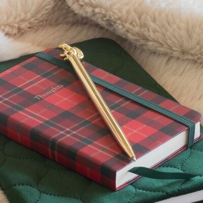 Caderno em padrão xadrez vermelho e preto com caneta dourada sobre tecido verde acolchoado