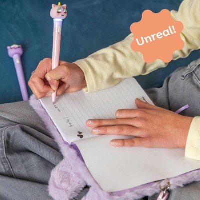 Pessoa a escrever num caderno com caneta decorada com cabeça de gato unicórnio cor-de-rosa