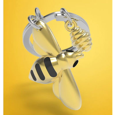 Chaveiro dourado e prateado em forma de abelha com pingente de favo de mel em fundo amarelo