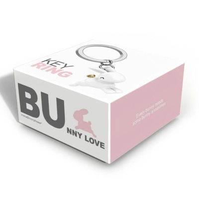 Chaveiro em forma de cão branco numa caixa branca e rosa com texto