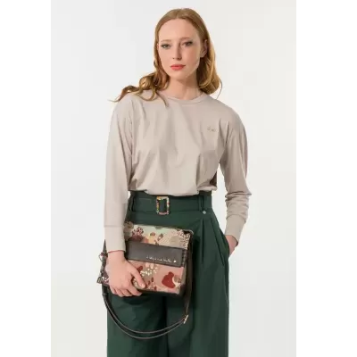 Mulher com camisola bege e calças verdes segurando mala de mão estampada