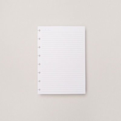 Folha branca pautada com orifícios para encaixe em caderno, sobre superfície cinza