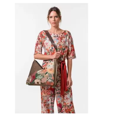 Mulher a usar mala de ombro triangular floral multicolorida com alça castanha e macacão estampado colorido