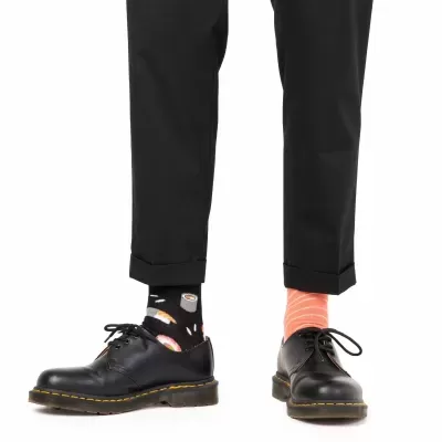 Pés com meias coloridas diferentes, sapatos pretos e calças pretas.