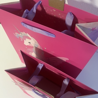 Duas sacolas cor-de-rosa com alças lilás e imagem de unicórnio