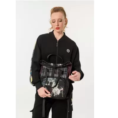 Mochila com padrão geométrico em tons azul, bege e roxo, segurada por mulher de casaco preto.