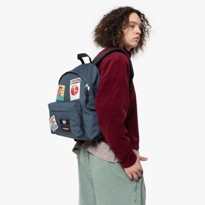 Mochila azul-escura com patches coloridos numa pessoa com camisola vermelha