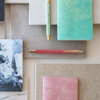 Cadernos com capas coloridas e esferográficas sobre mesas cinzentas e beges