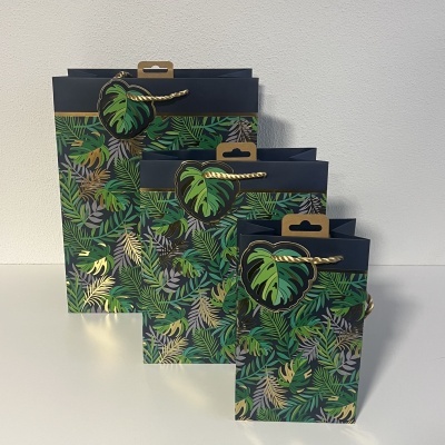Conjunto de três sacos de papel com padrão de folhas tropicais e cabos de corda dourada
