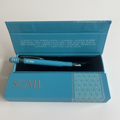 Caneta azul com nome SONIA numa caixa azul com tampa aberta e frase em português