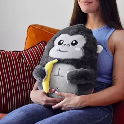 Pelúcia de gorila cinzento com banana na mão, segurada por mulher sentada no sofá