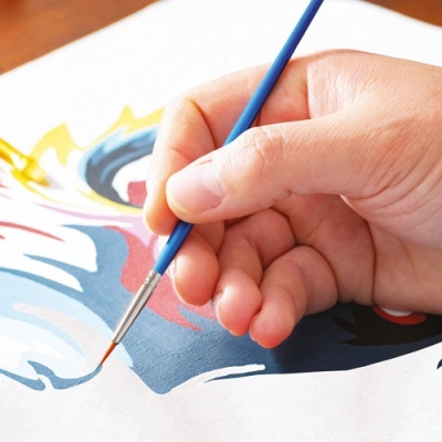 Mão a pintar padrão colorido em tecido branco com pincel azul.