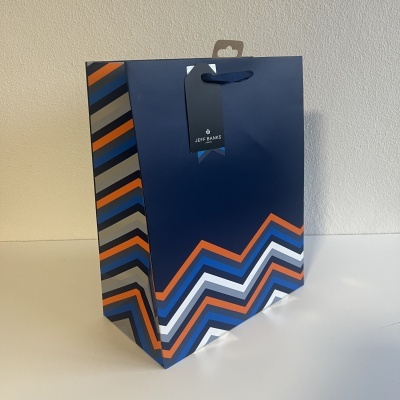 Saco de papel azul com padrão em ziguezague colorido e etiqueta JEFF BANKS