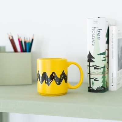Caneca amarela com padrão preto numa prateleira com livros e lápis