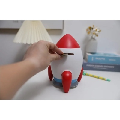Poupança em forma de foguetão vermelho, branco e azul com uma mão a colocar moeda