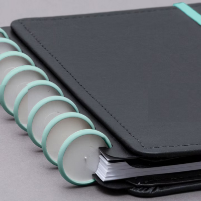 Caderno preto com espiral e fecho azul claro sobre superfície cinzenta