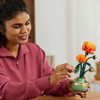 Mulher a montar flor de LEGO laranja num vaso verde em mesa de madeira