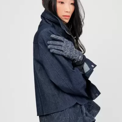 Mulher vestindo casaco azul escuro, camisa azul com letras brancas e luvas cinza com padrão floral