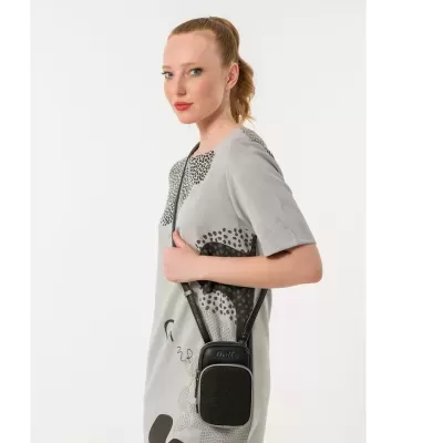 Mulher com vestido cinzento e bolsa preta de alça comprida em fundo branco