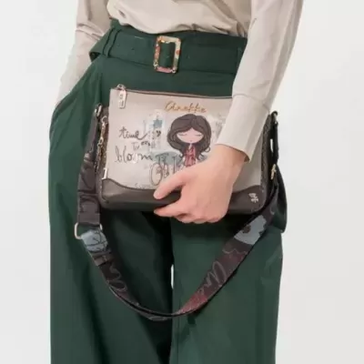 Bolsa bege e castanha com alça preta e padrão floral, ilustrada com rapariga e texto, usada com roupas verdes e bege.