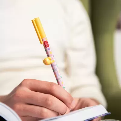 Caneta amarela decorada com flores e personagem amarelo a ser usada para escrever num caderno.
