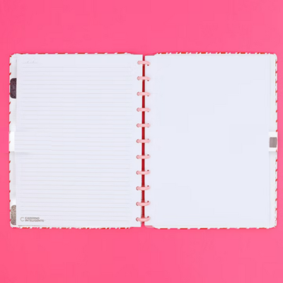Caderno aberto com folhas pautadas e brancas sobre fundo rosa