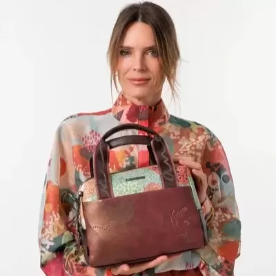 Mala pequena de mão castanha e colorida segurada por mulher com blusa colorida