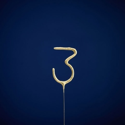 Vela dourada em forma do número 3 com fundo azul escuro