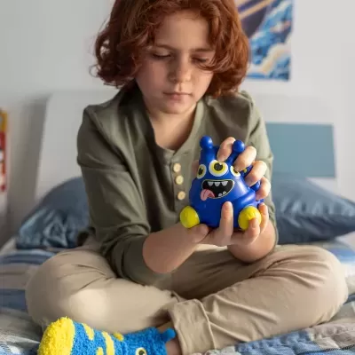 Criança com brinquedo de monstro azul sentado numa cama