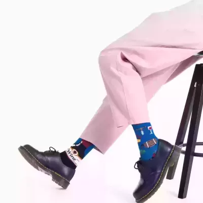 Pessoas com meias azuis estampadas, calças rosa e sapatos pretos sentadas num banco preto.